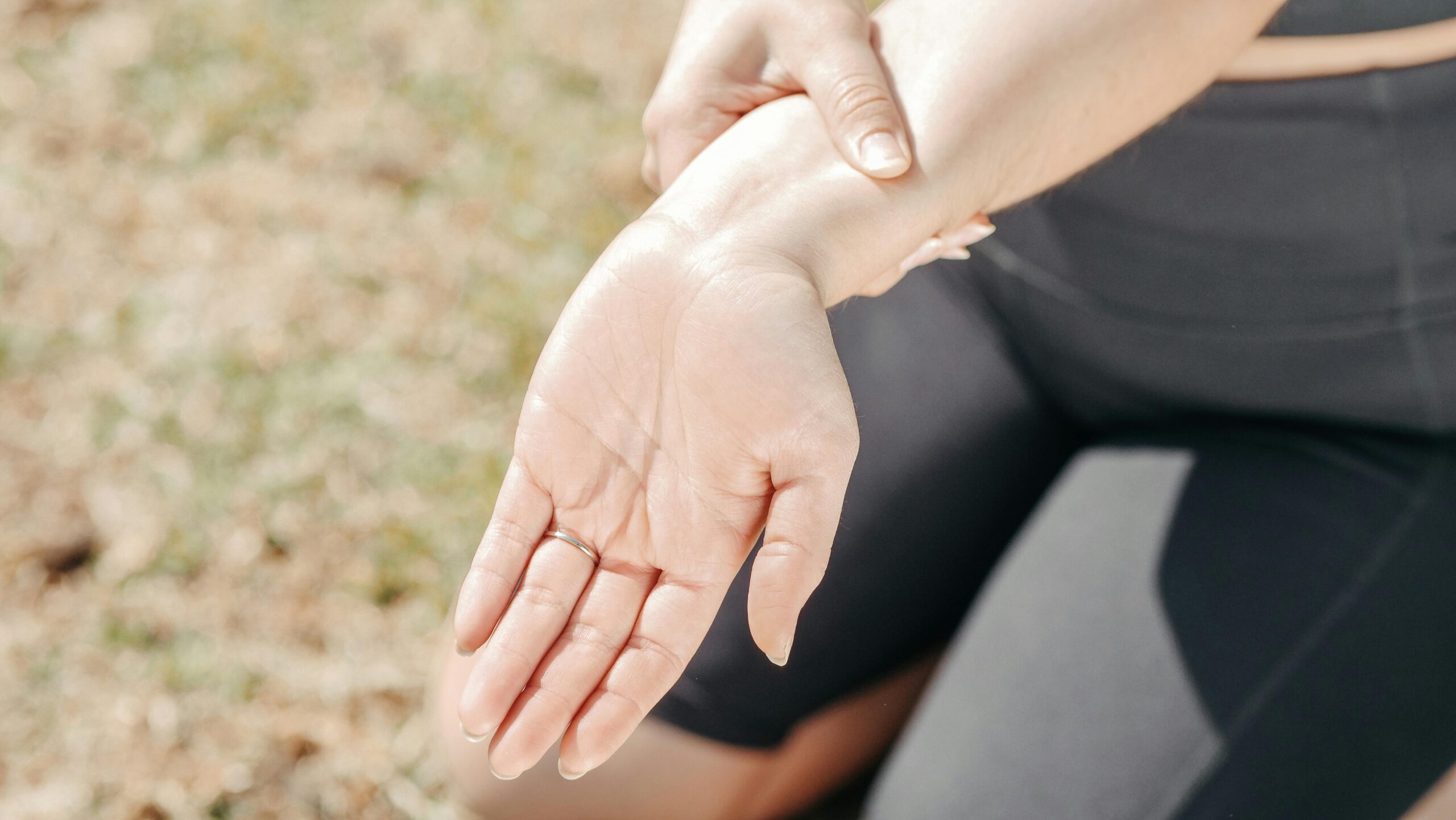Person gripping wrist in pain, highlighting injury and support outdoors.